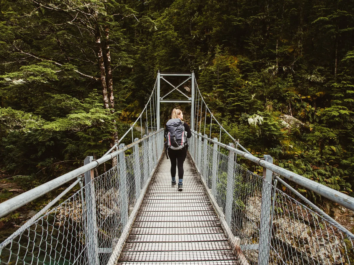 Hiker walking across swing bridge in the National Park, Routeburn Track, Fiordland Outdoors